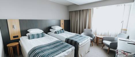 A hotel room with two beds, a desk, a chair, and a small stool.