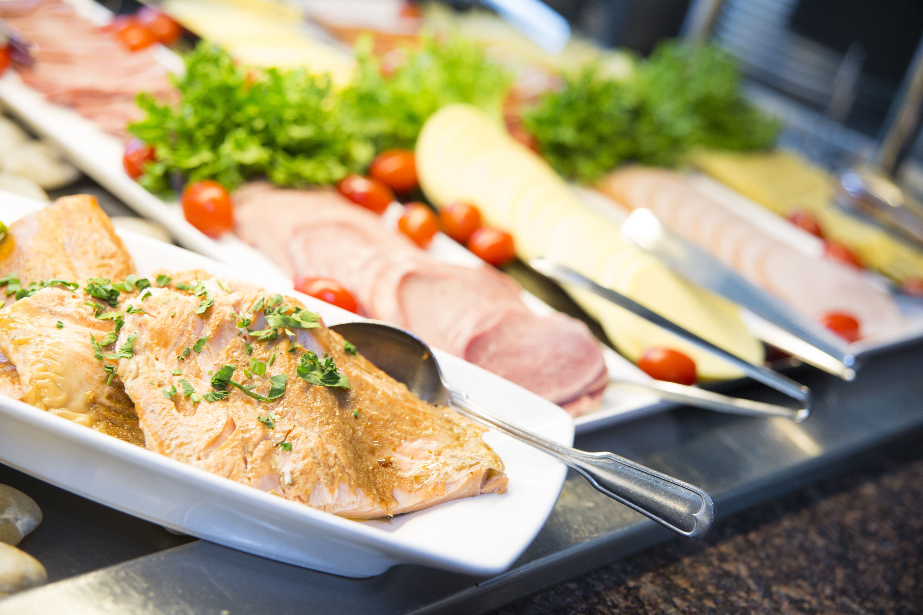 A buffet with various food items including salmon, ham, and cheese.