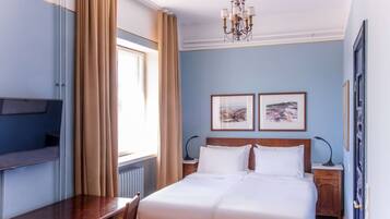 A hotel room with a bed, a desk, a chair, a TV, and two framed pictures on the wall.