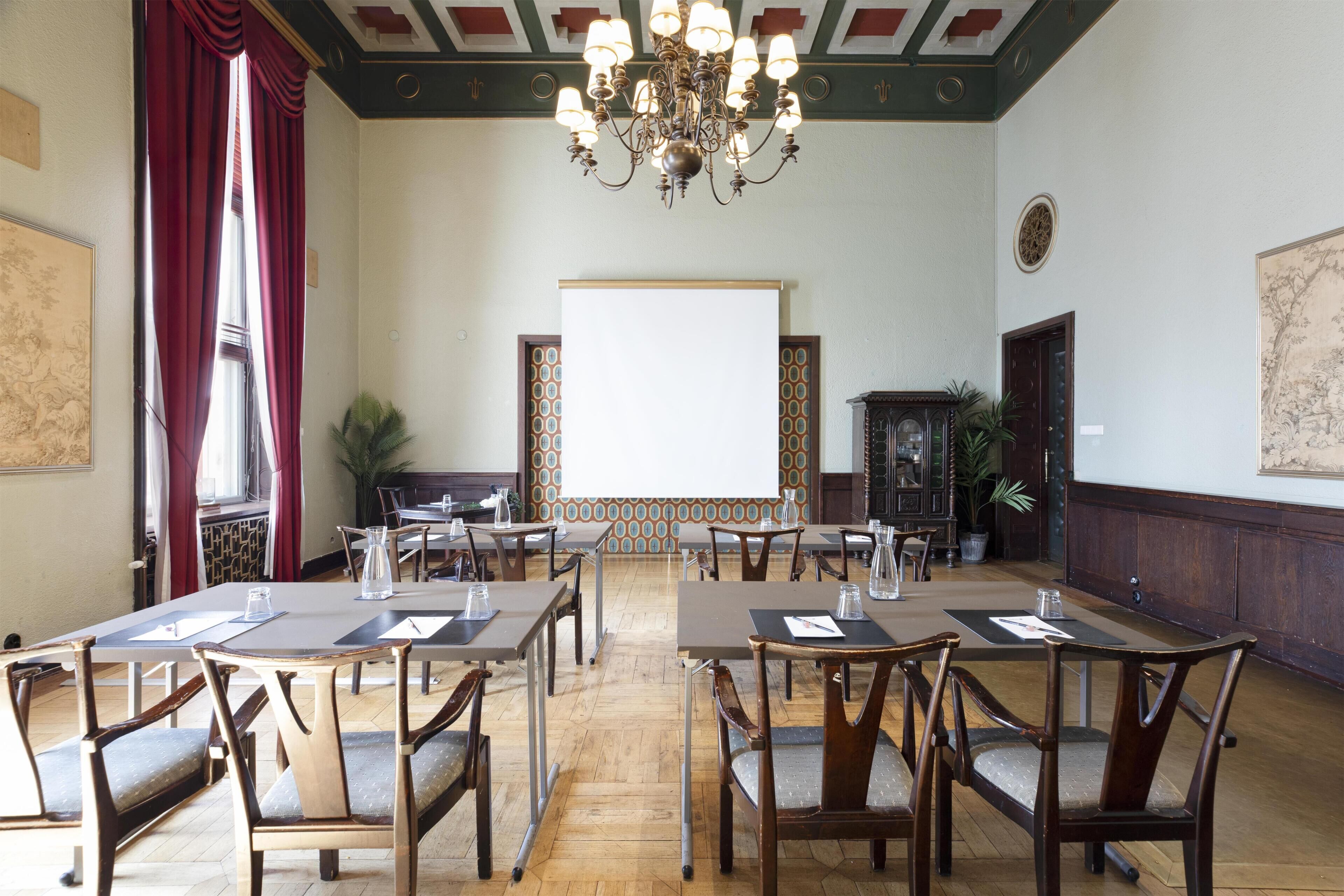 Un salón de conferencias con mesas y sillas de madera, una lámpara de araña y una pizarra.
