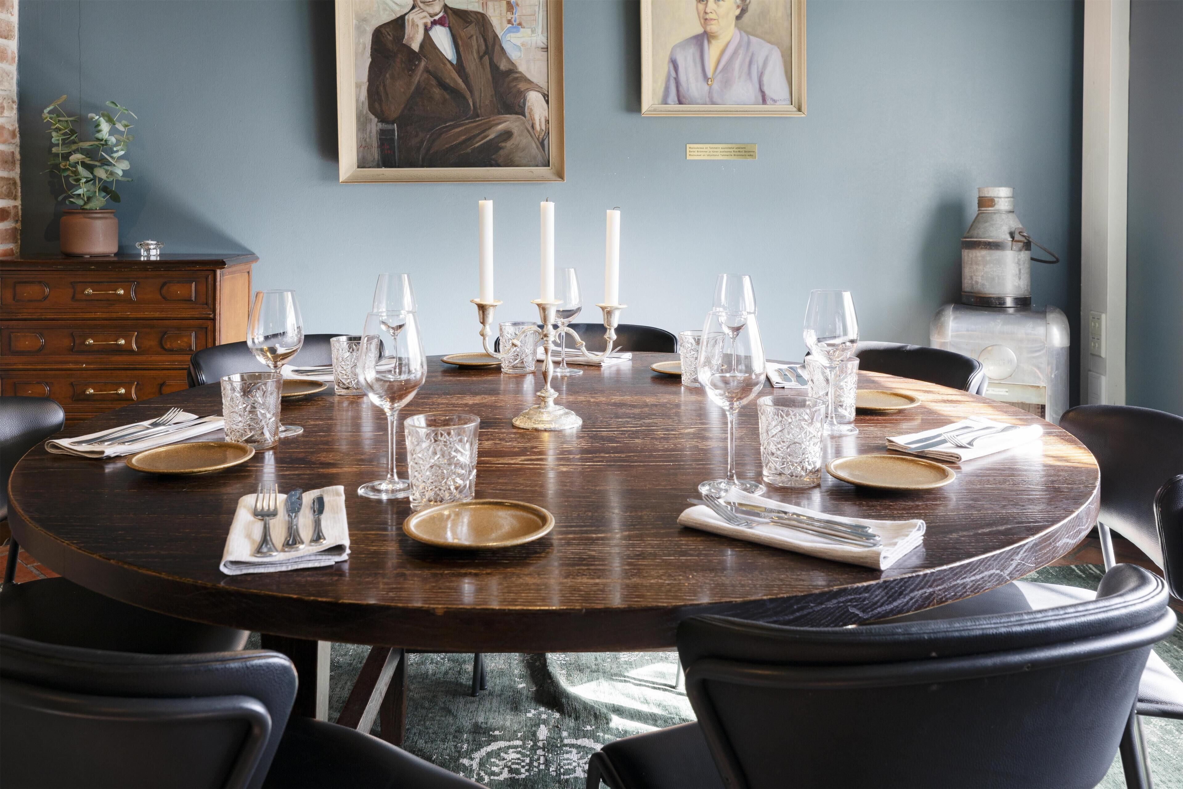 Een ronde eettafel gedekt met kaarsen, borden en bestek, omringd door stoelen.