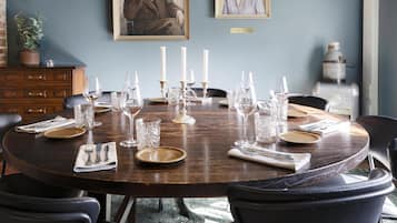 Een ronde eettafel gedekt met kaarsen, borden en bestek, omringd door stoelen.