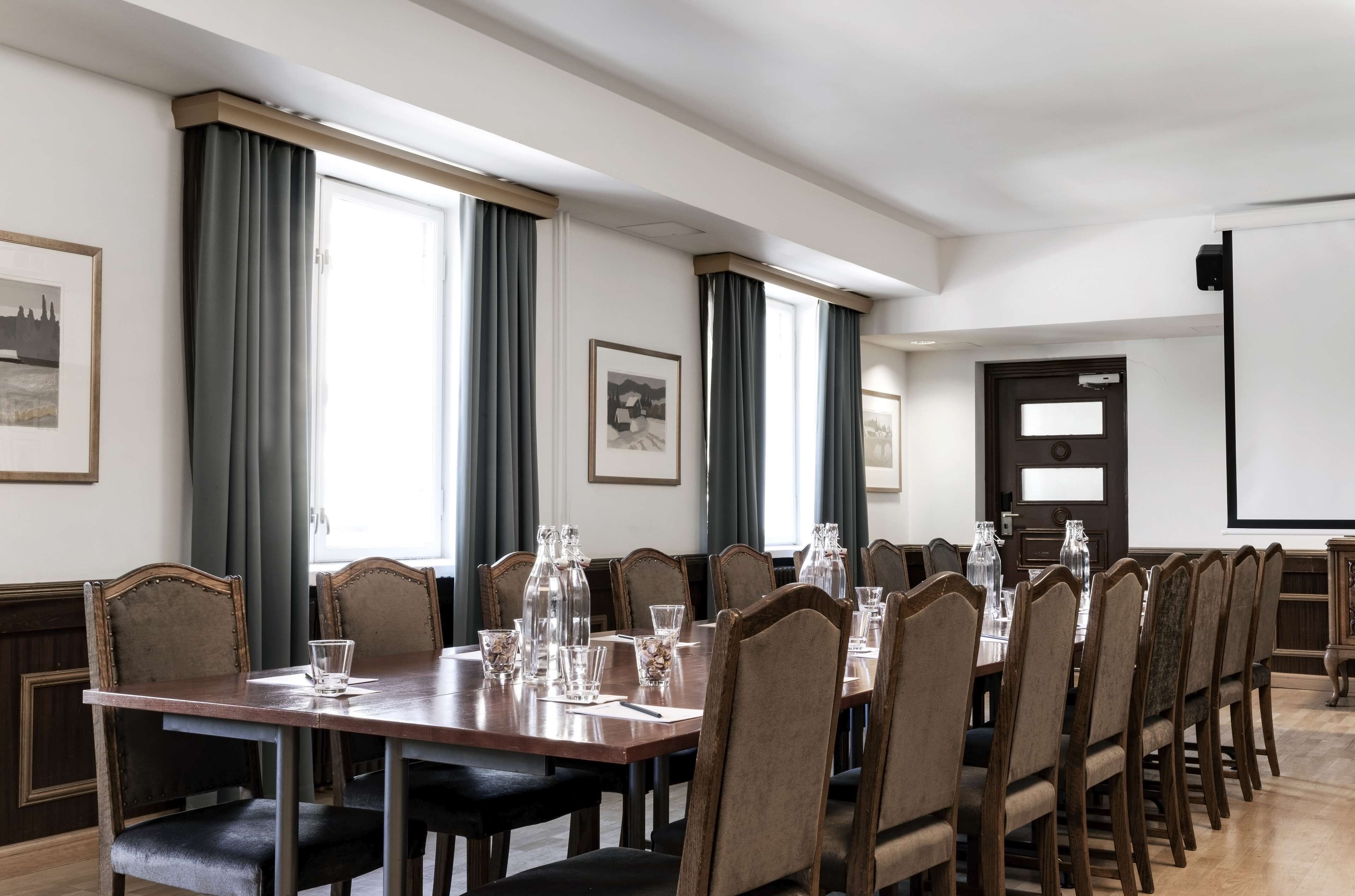 A conference room with a long table, chairs, and a projector screen.