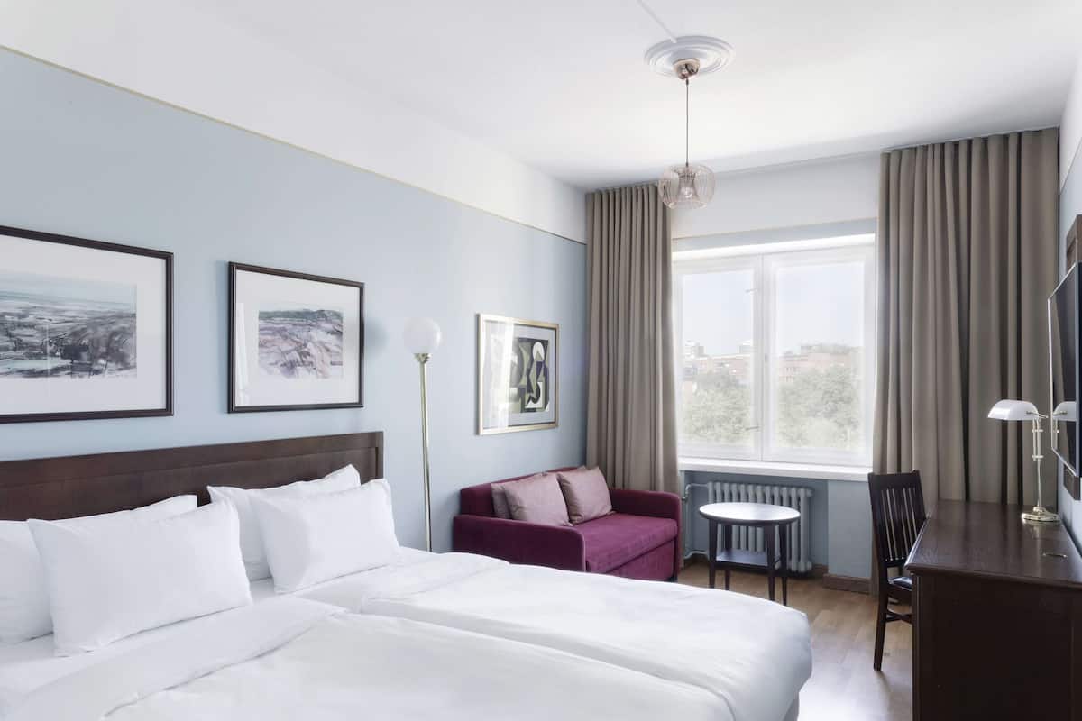 Una habitación de hotel con una cama grande, un sofá, un escritorio y una ventana con cortinas.