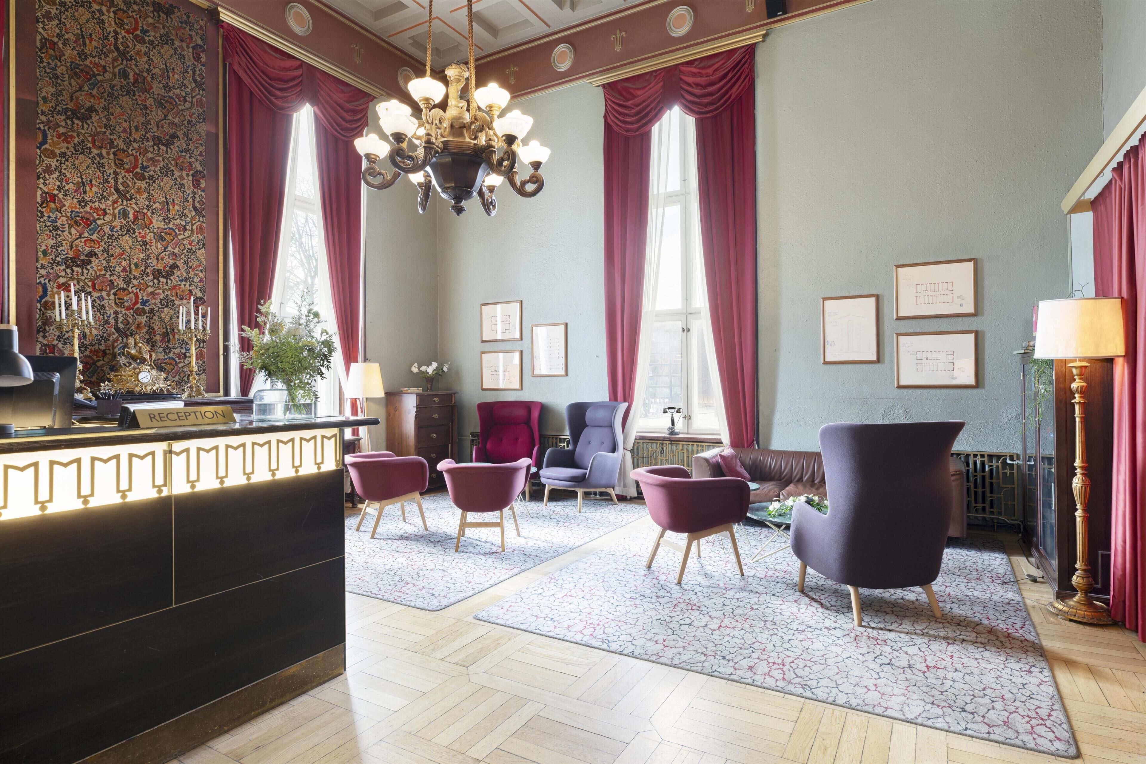 A reception area with a reception desk, a chandelier, and a seating area with chairs and a sofa.