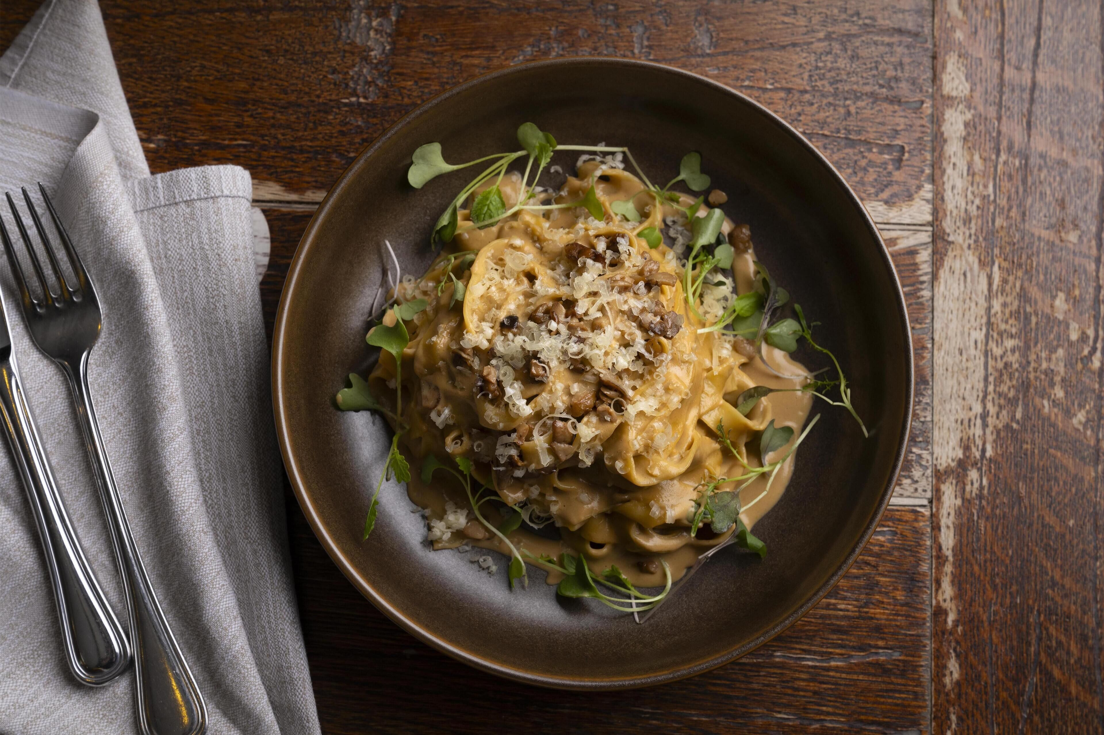Een bord pasta met champignons en groenten op een donker bord.