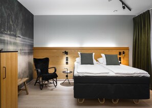A modern hotel room with a wooden headboard, a black chair, a small round table, and a bed with white bedding and two pillows.