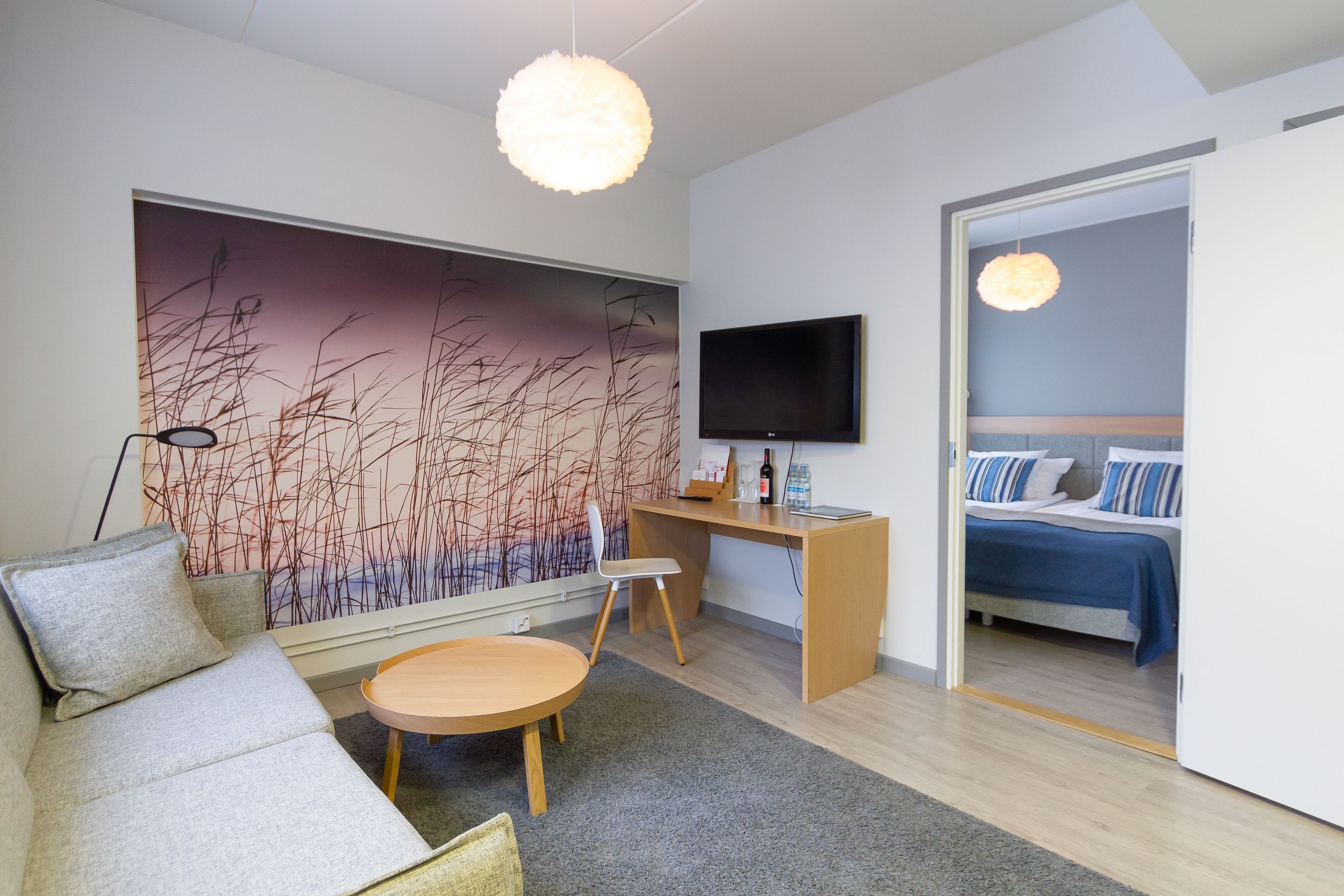 A modern hotel room with a sofa, round table, and a desk with a TV.