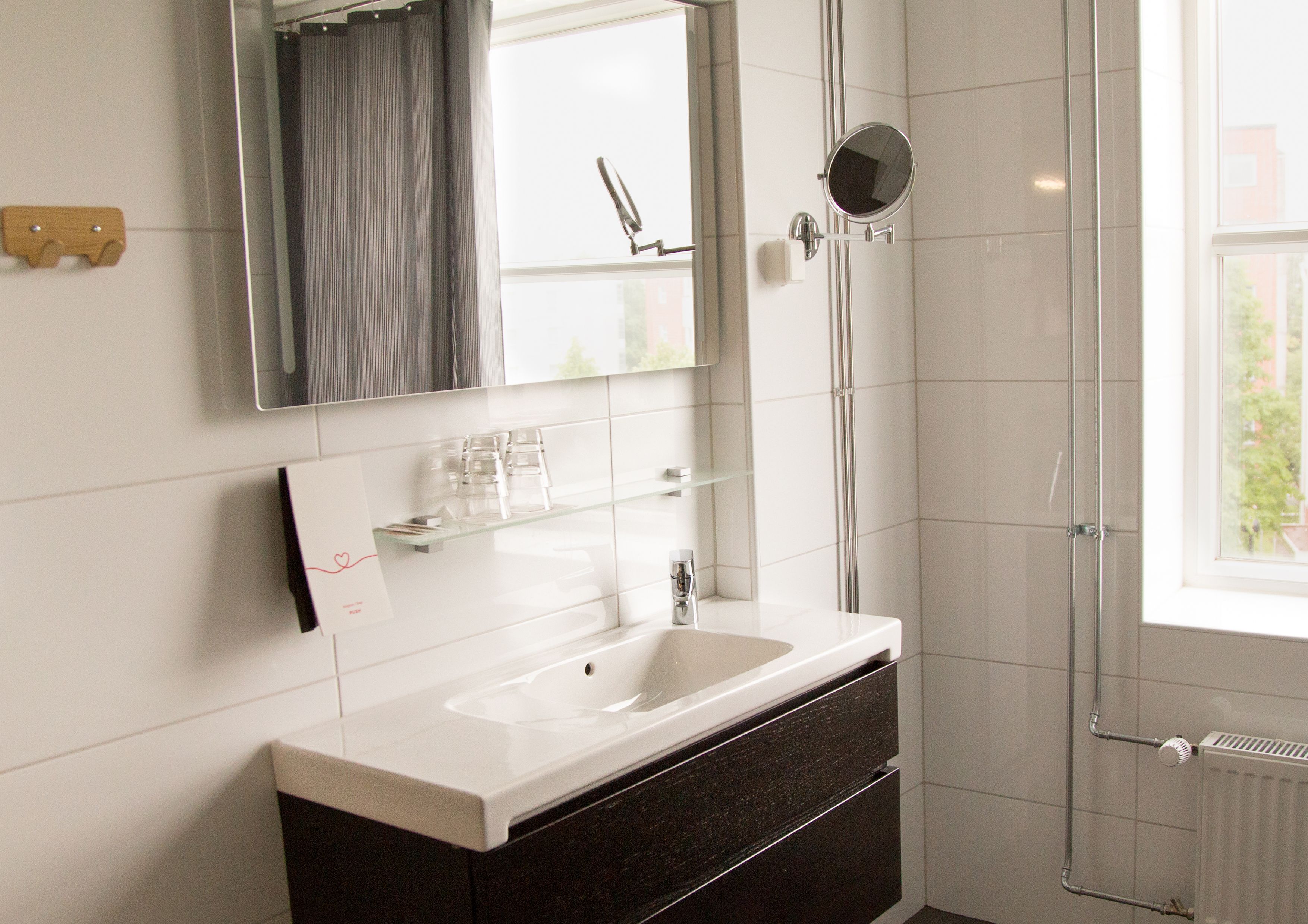 Une salle de bain moderne avec un lavabo blanc, des meubles de rangement aux couleurs sombres, une douche en verre et un grand miroir.