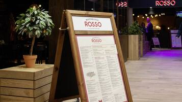 A restaurant menu board for Ristorante Rosso, featuring a wooden stand and a potted plant.