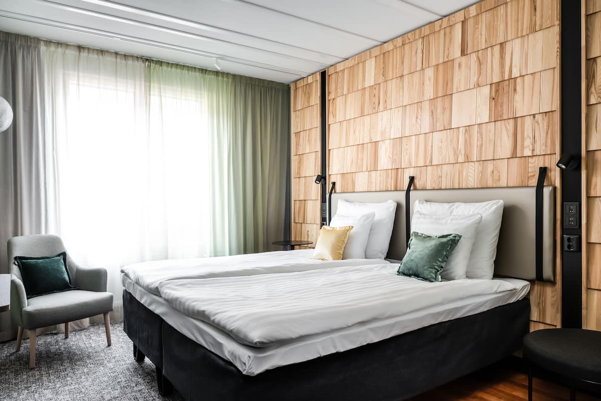 Une chambre d’hôtel moderne avec un grand lit, une chaise et un mur recouvert de panneaux en bois.
