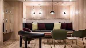 En modern inredning med en väggpanel i trä, en svart soffa med flera kuddar och ett runt bord med stolar.