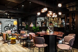 Een moderne barruimte met ronde tafels, zachte stoelen en hanglampen.