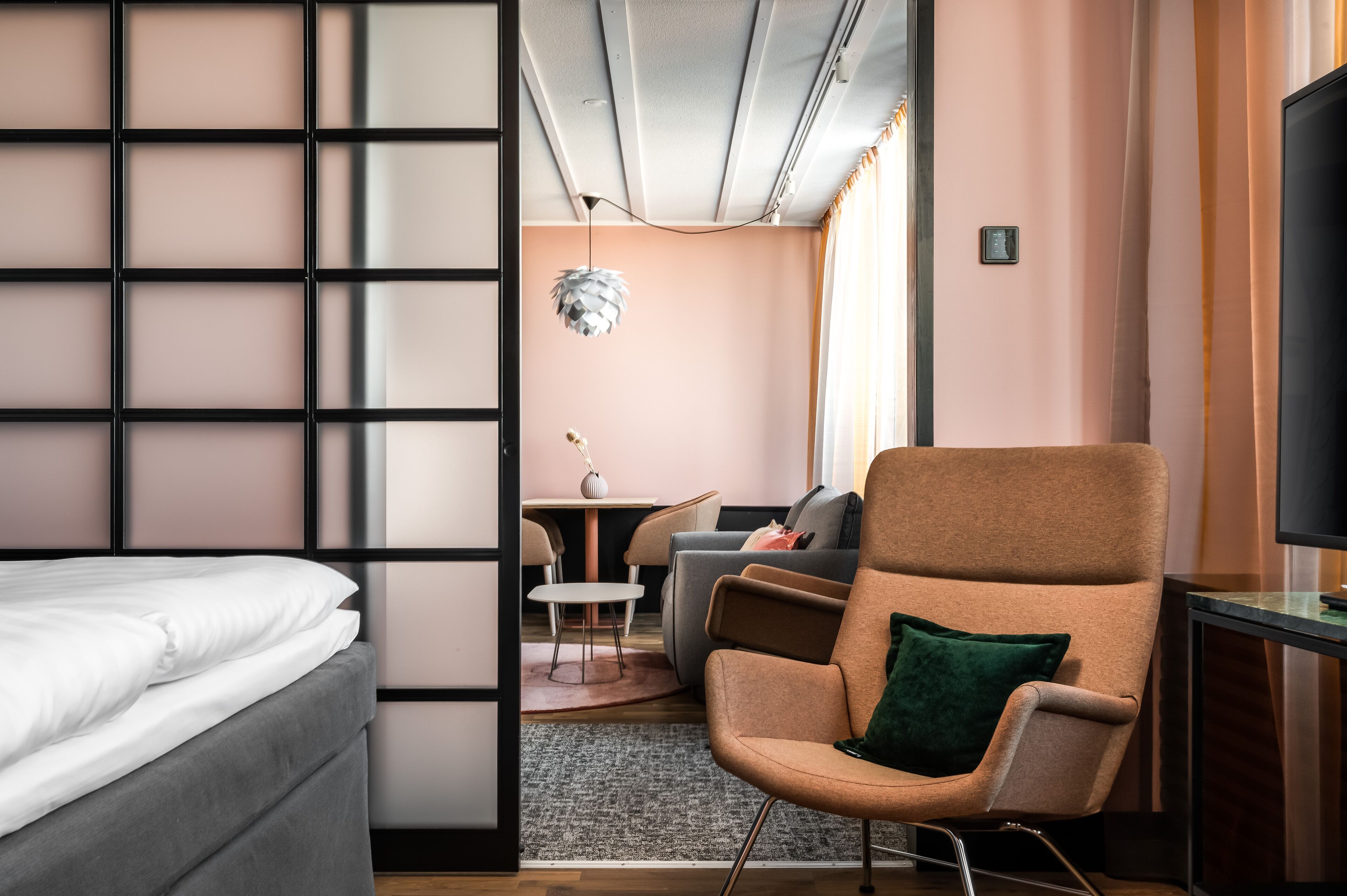 Ett modernt hotellrum med en säng, en sittgrupp med soffa och fåtöljer, ett litet bord och en tv.