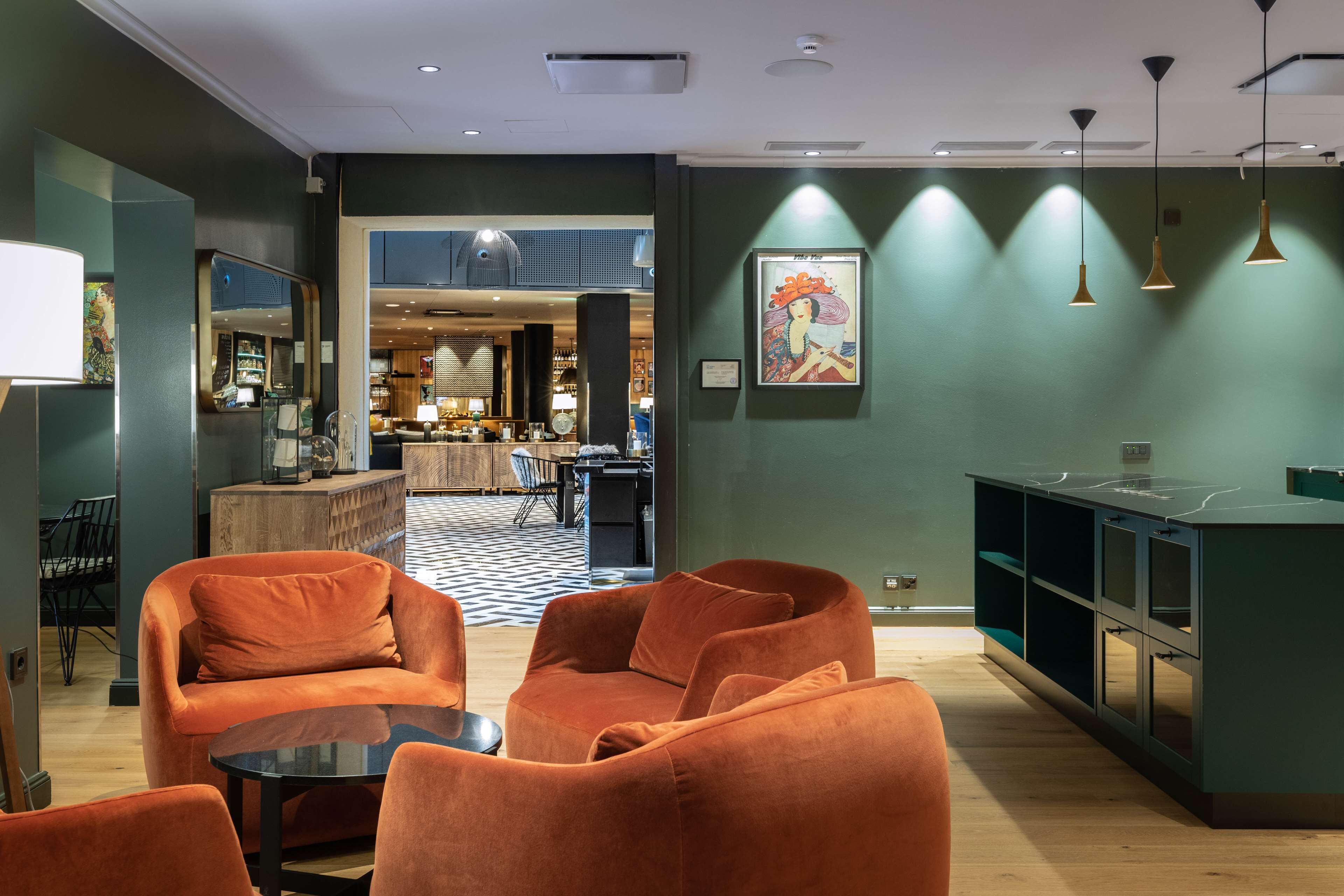 A modern hotel lobby with orange seating, a bar area, and a view into the dining space.