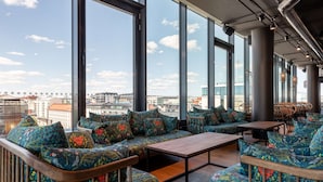 Un salón con techos altos, amplias ventanas que ofrecen vistas a la ciudad, asientos con diseños y conductos expuestos.