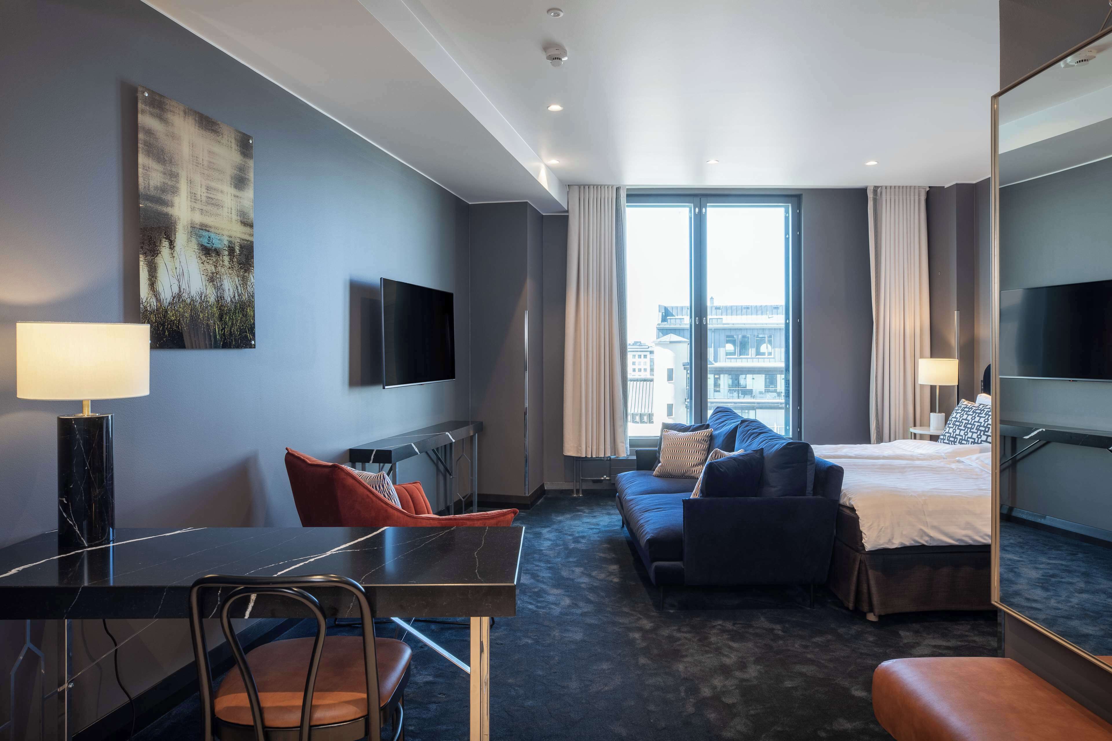 Una habitación de hotel moderna con cama, sofá, escritorio y televisión.