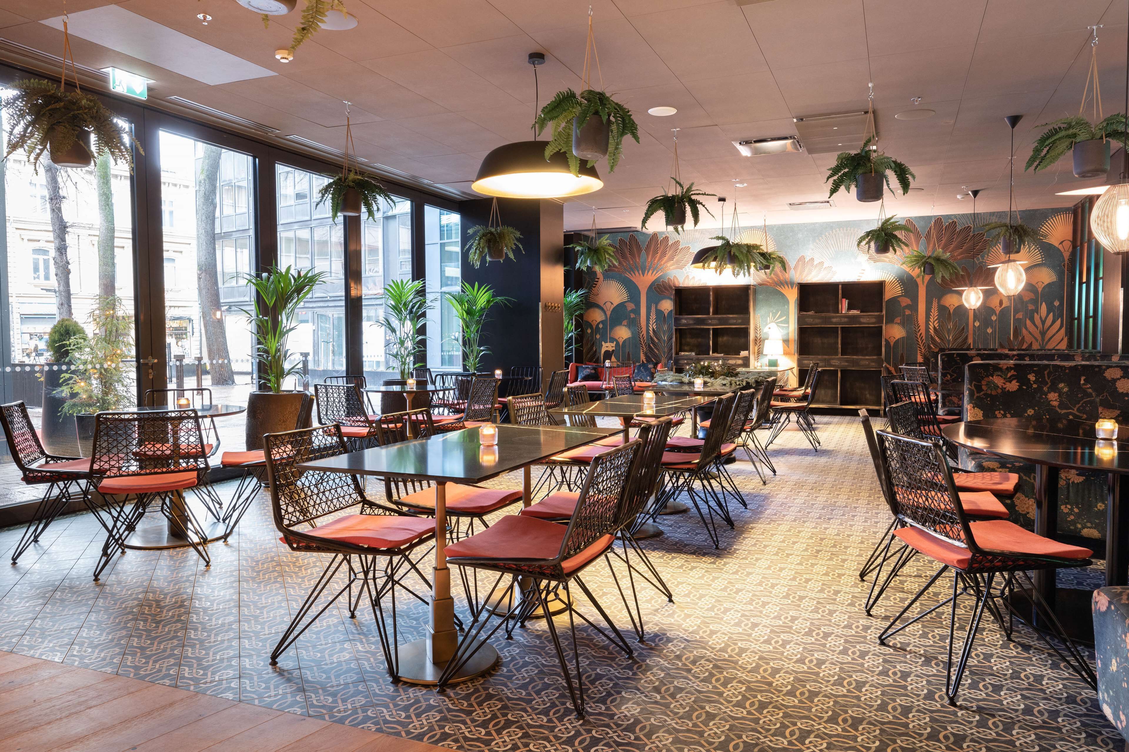 Un amplio comedor interior con varias mesas y sillas, ventanas grandes y plantas colgantes.