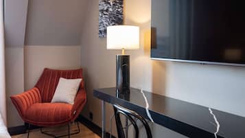 Una habitación de hotel moderna con una butaca tapizada de rojo, un escritorio negro con una lámpara y un televisor de pantalla plana grande montado en la pared.