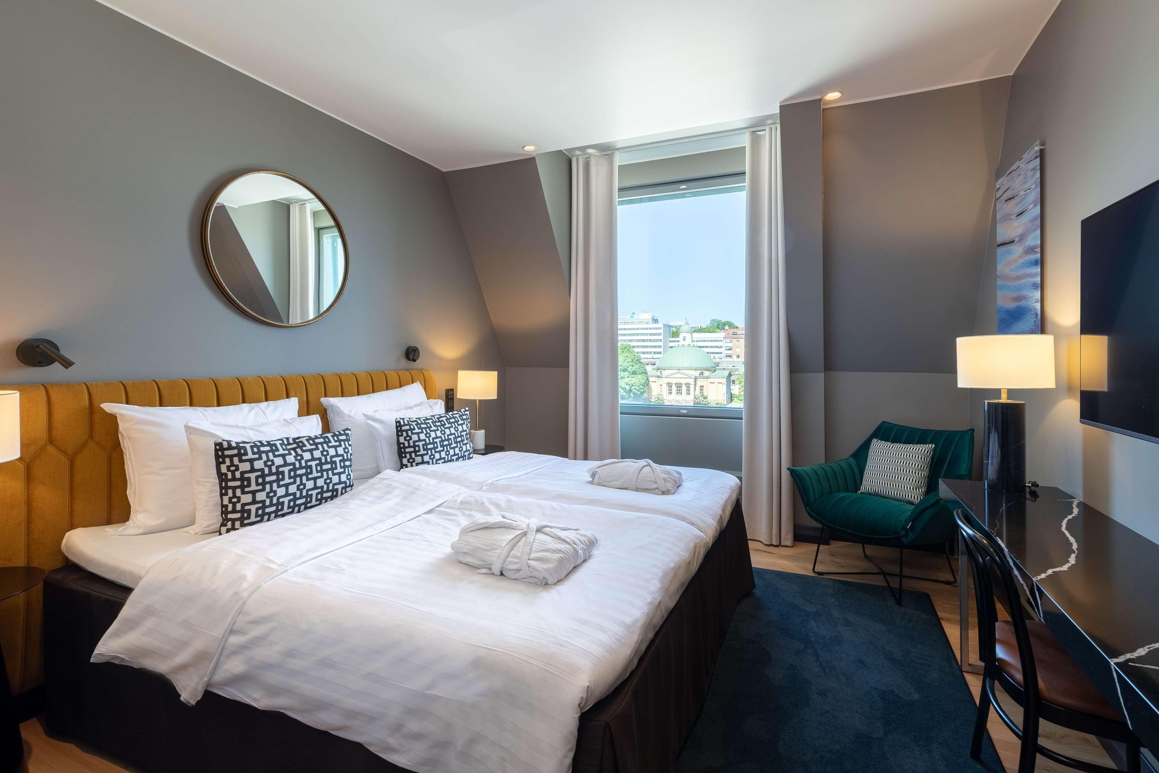 A hotel room with a bed, a chair, a desk, a TV, and a window with a view.
