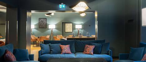 Un área lounge moderna con sofás y sillones azules, una mesa de centro de vidrio y un comedor al fondo.