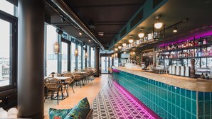 Zona de bar con una barra larga, asientos y vistas a través de amplios ventanales.
