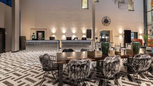 Un moderno vestíbulo de hotel con un mostrador de recepción, una amplia mesa de comedor con sillas y un piso con estampado.