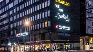 Un edificio moderno con un cartel grande que dice 'AMARILLO' y 'SEURAHUONE' hotel. Hay escaparates de vidrio con áreas de estar visibles.