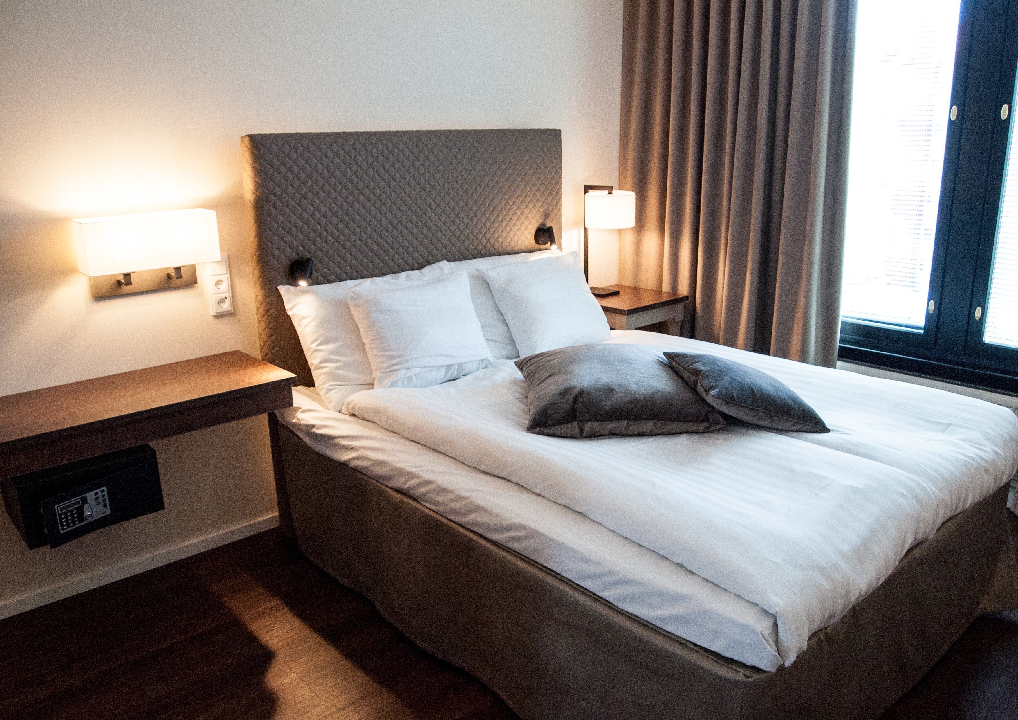 A neatly made bed with white and gray bedding, a headboard, bedside lamps, and a nightstand with a power outlet.