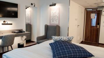 Habitación de hotel con cama, escritorio y silla, televisor montado en la pared y puerta que da a otra habitación.