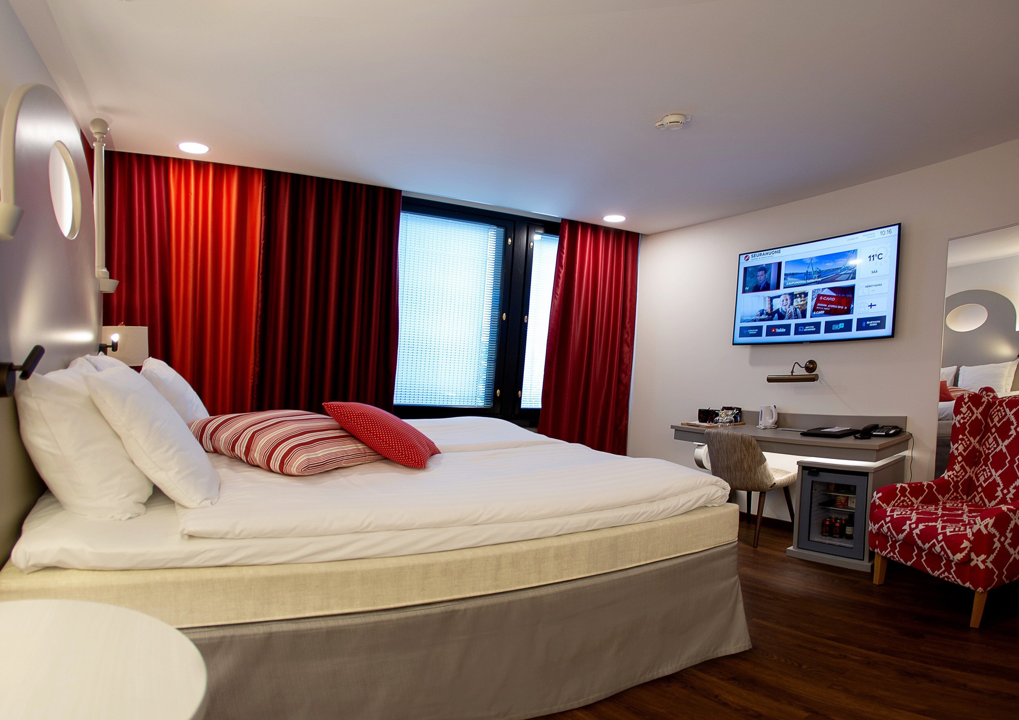 A modern hotel room with a large bed, a desk, and a television.