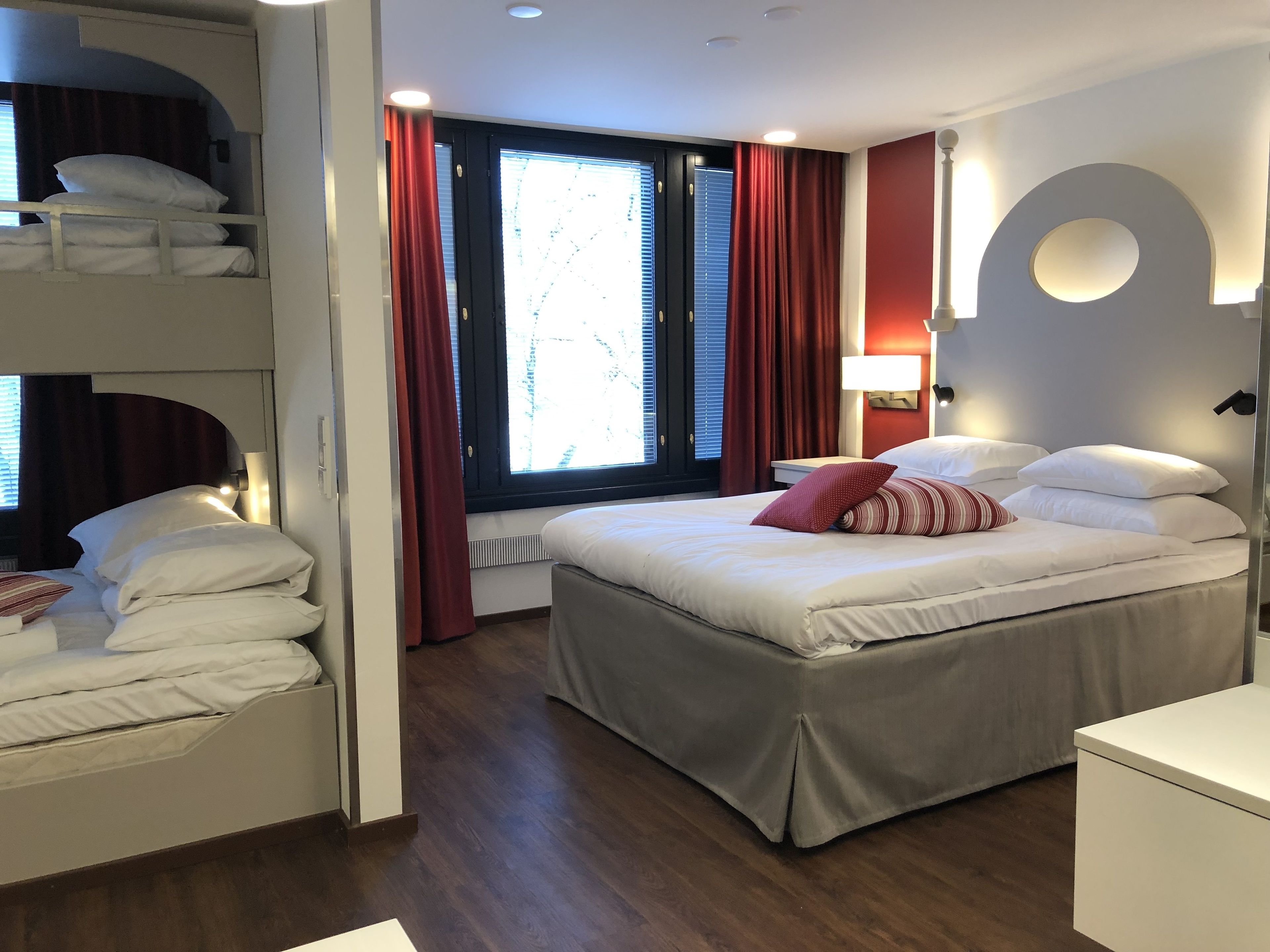 A hotel room with a bed, a desk, a wardrobe, and a window with curtains.