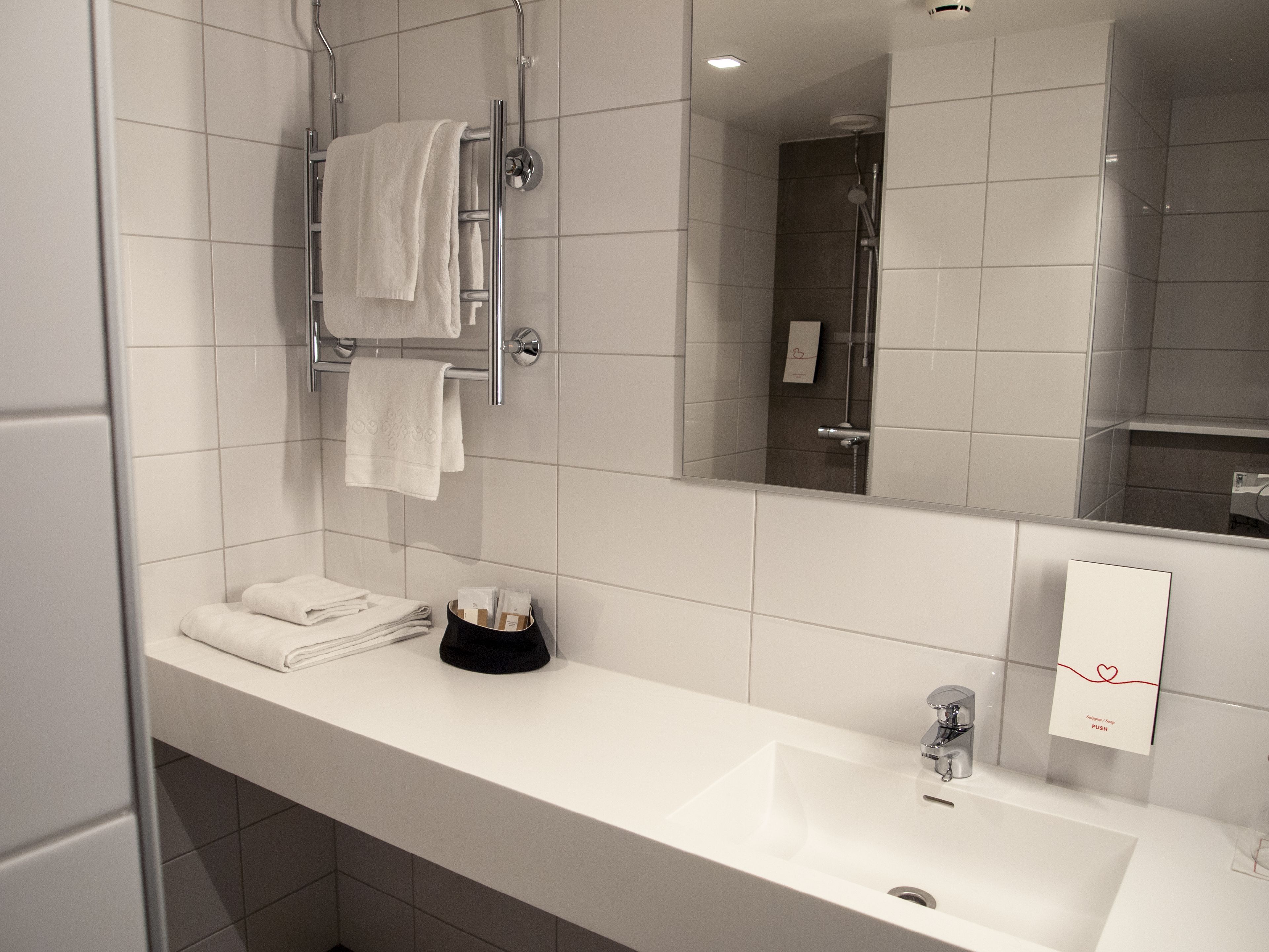 A modern bathroom with a white sink, a mirror, and a towel rack.