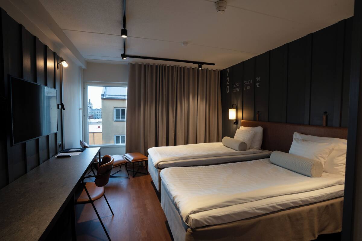 Habitación de hotel con dos camas, un escritorio, una silla, un televisor y una ventana con cortinas.