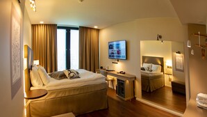 Una habitación de hotel con cama, escritorio, silla, espejo grande y televisor.