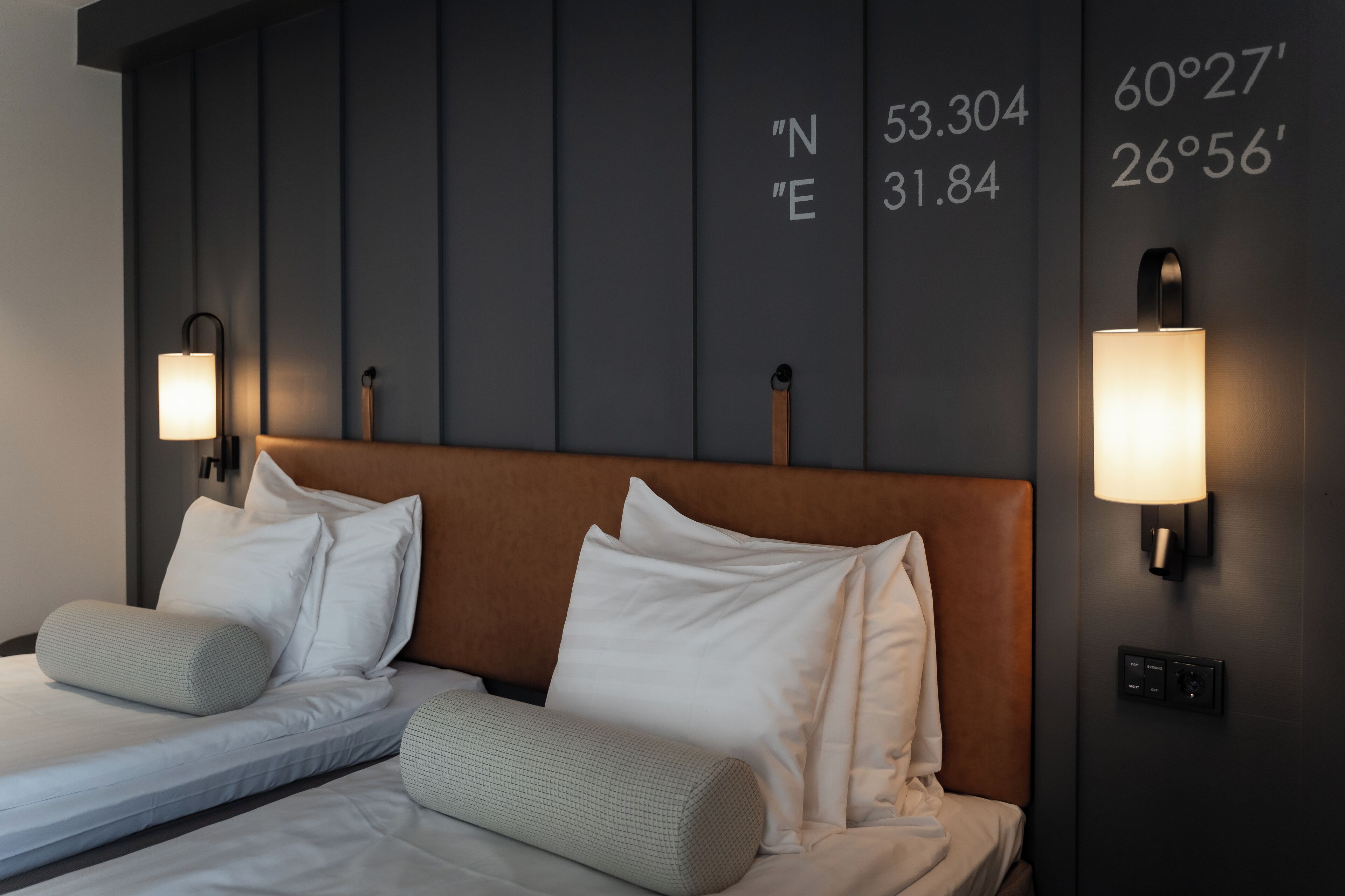 Habitación de hotel con una cama grande, dos mesitas de noche y una pared con coordenadas.