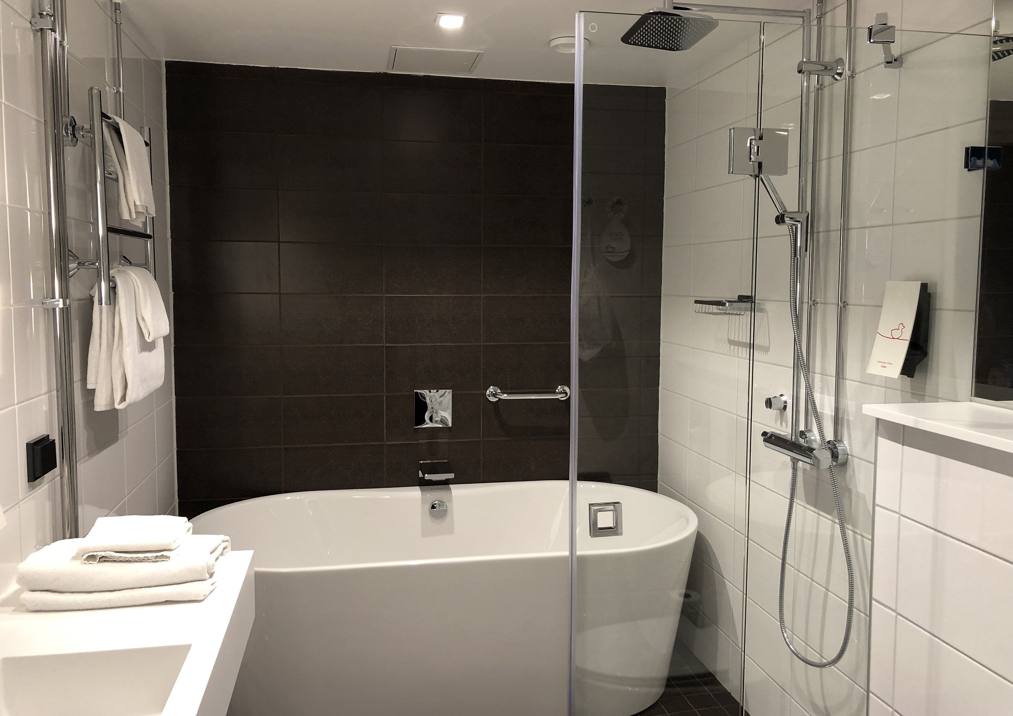 Un baño moderno con una bañera independiente, ducha con cerramiento de vidrio y un mueble de tocador blanco con toallas.