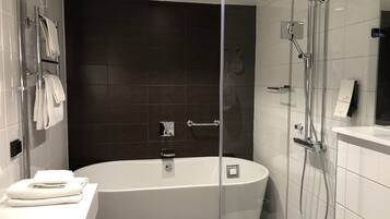 Un baño moderno con una bañera independiente, ducha con cerramiento de vidrio y un mueble de tocador blanco con toallas.