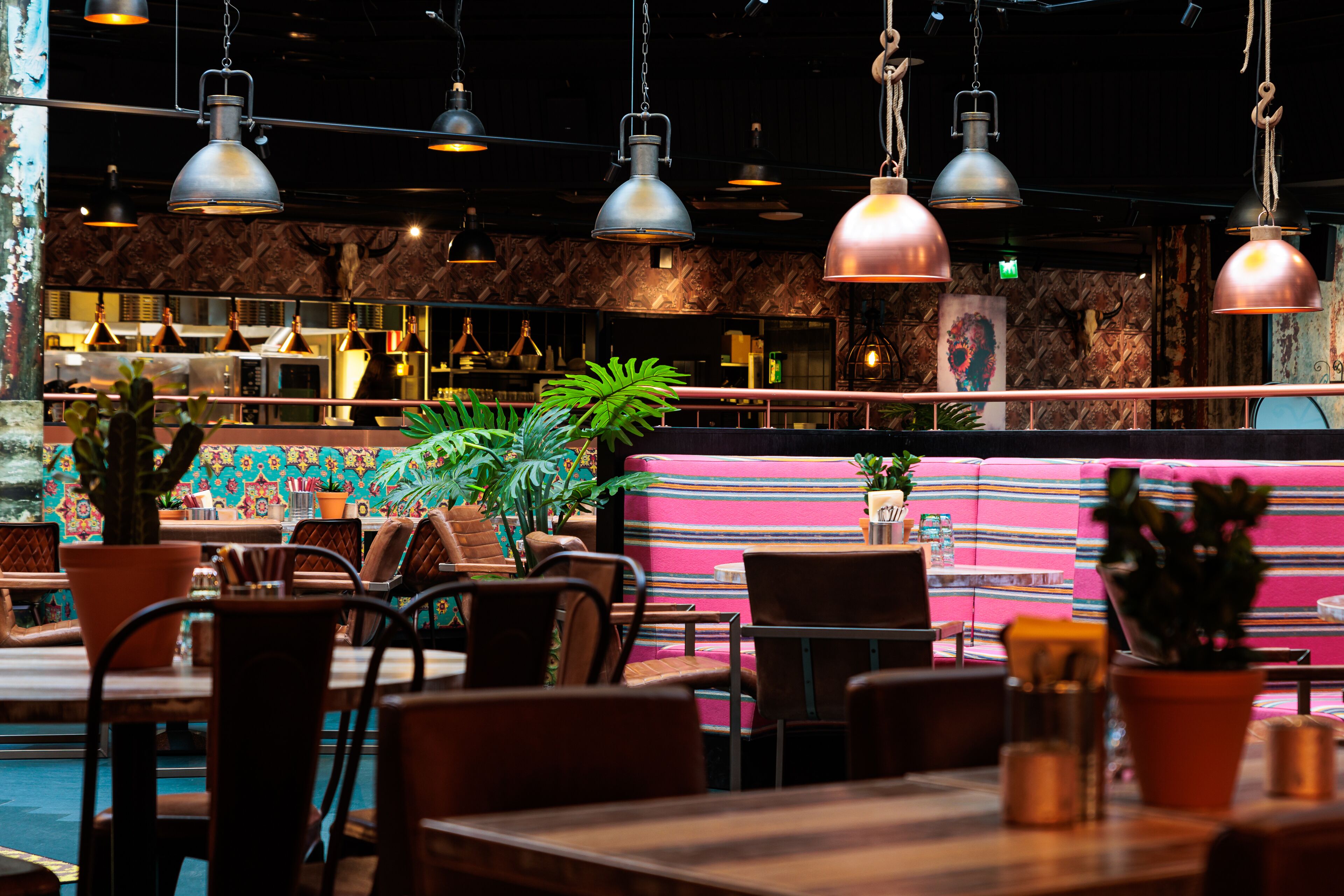 A restaurant with striped booths, hanging industrial-style pendant lights, and potted plants.