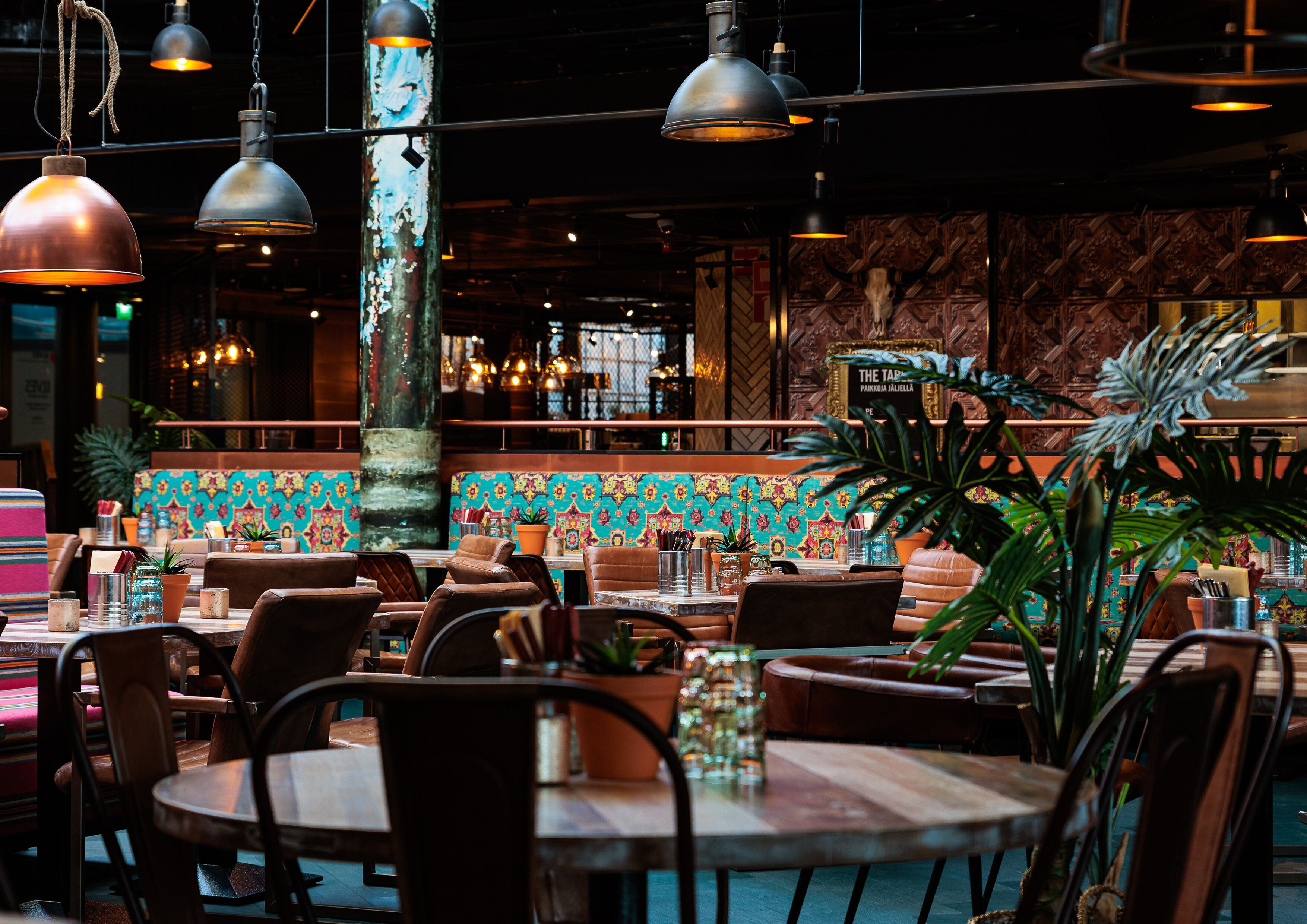 Un interior de restaurante con mesas y sillas de madera, lámparas colgantes y un vibrante salpicadero de azulejos.