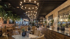 Um restaurante com móveis de vime, plantas em vasos e uma parede de tijolos.