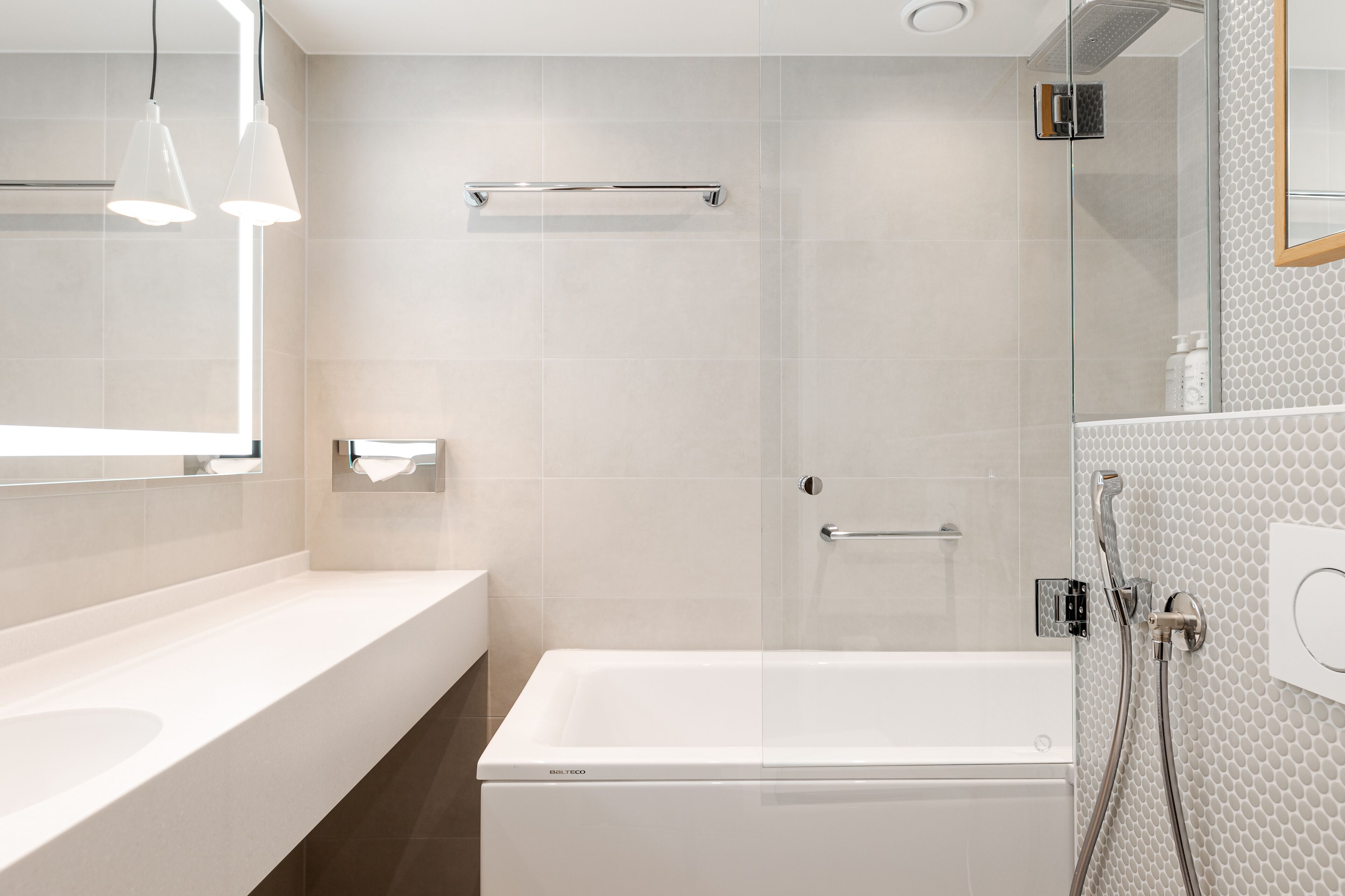 A modern bathroom with a white bathtub, a glass-enclosed shower, and a large mirror.