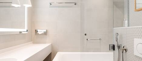 A modern bathroom with a white bathtub, a glass-enclosed shower, and a large mirror.