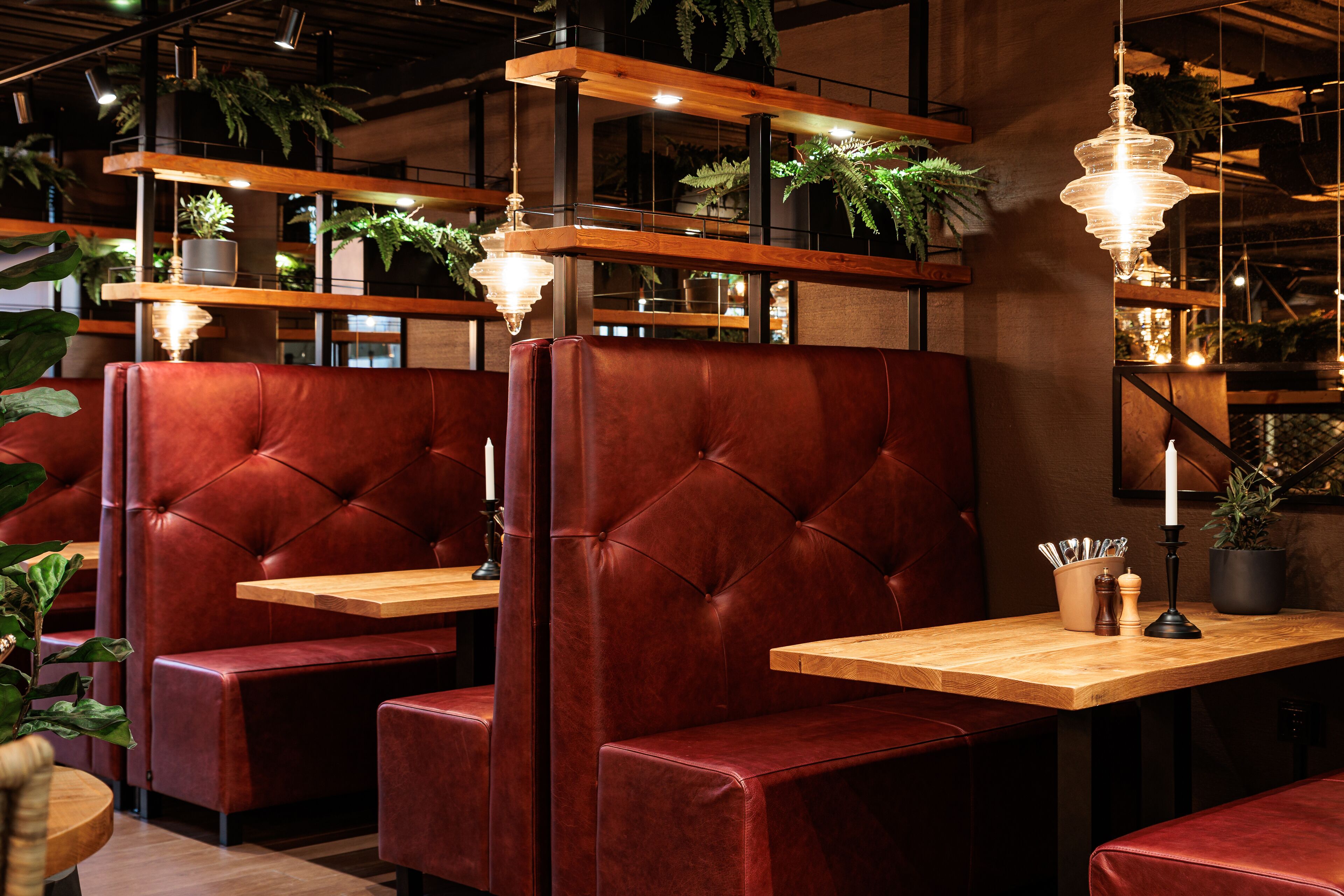 Un restaurant avec des banquettes en cuir rouge, des tables en bois, des plantes suspendues et des luminaires suspendus.