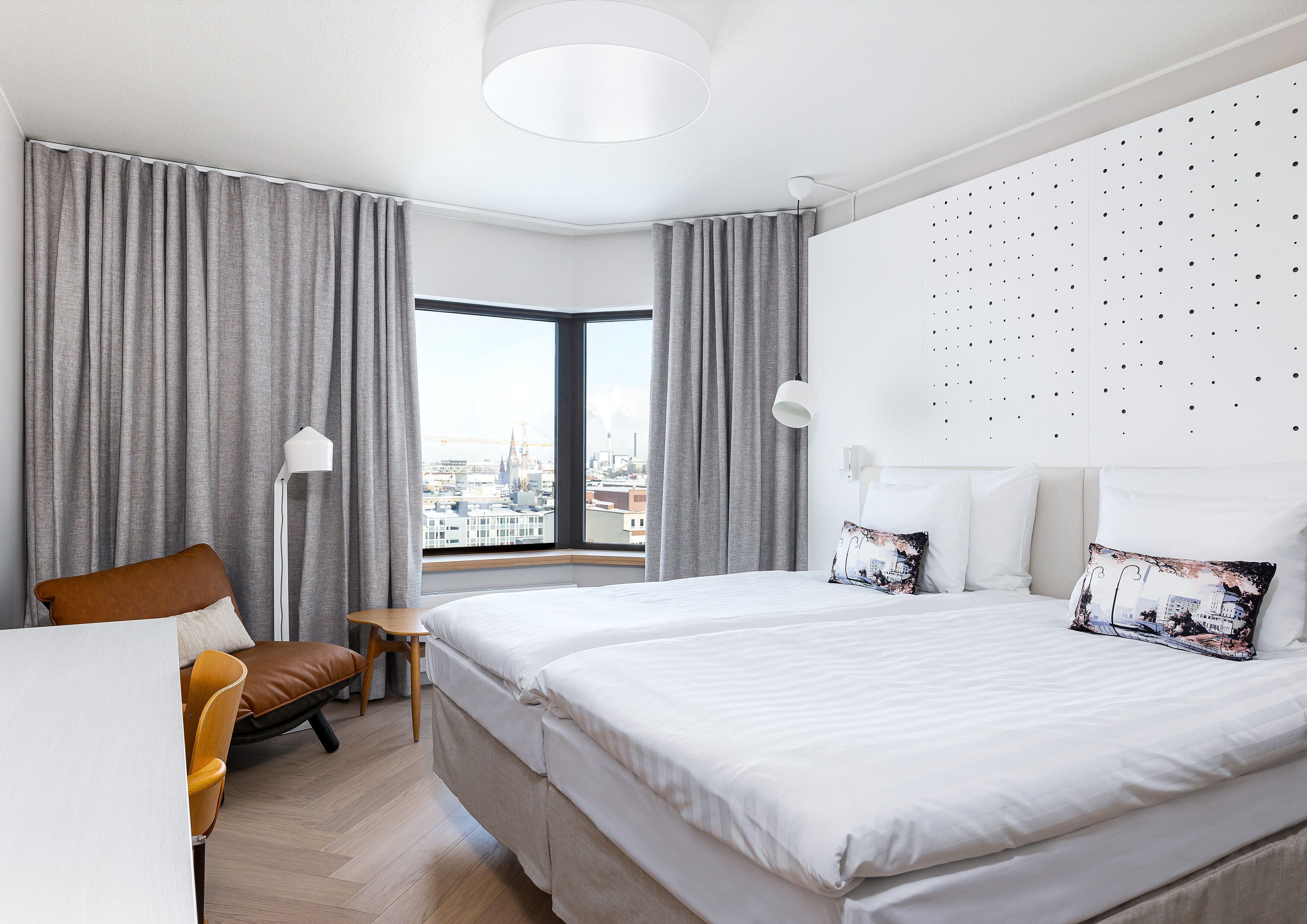 Habitación de hotel moderna con una cama grande, un escritorio y una silla. Se ve una ventana con vista a la ciudad.