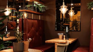 A cozy restaurant interior with leather booths, wooden tables, hanging pendant lights, and potted plants.