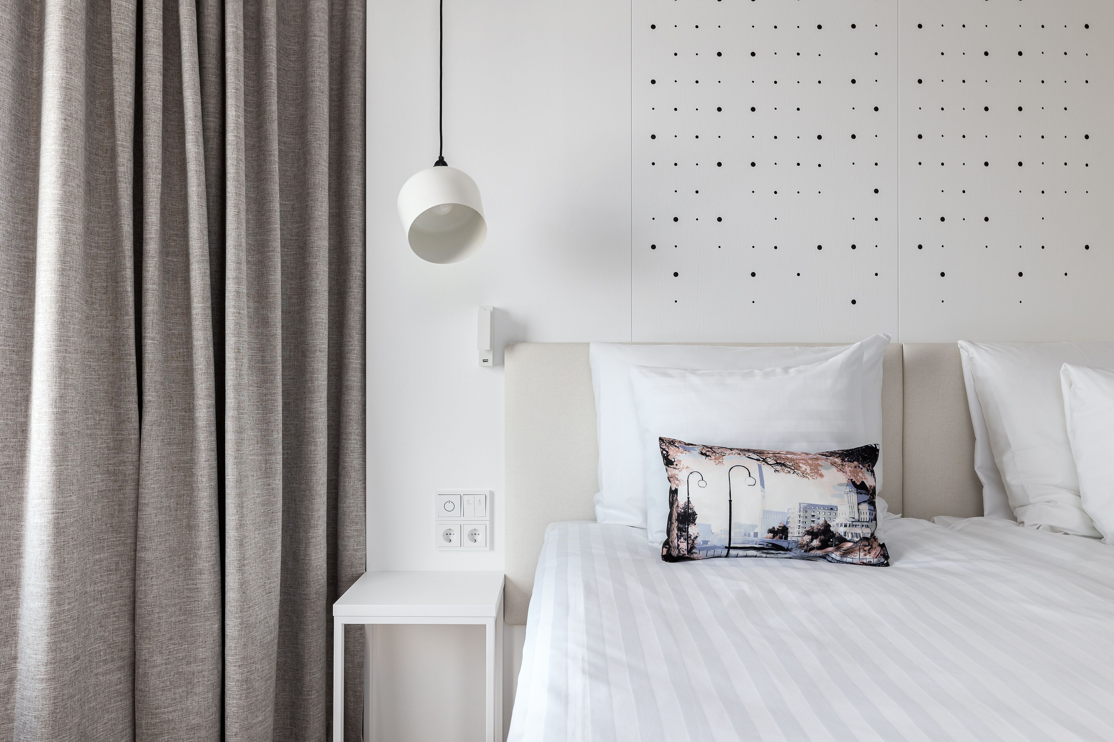 Een hotelkamer met een bed, nachtkastje, wandlamp en gordijn.