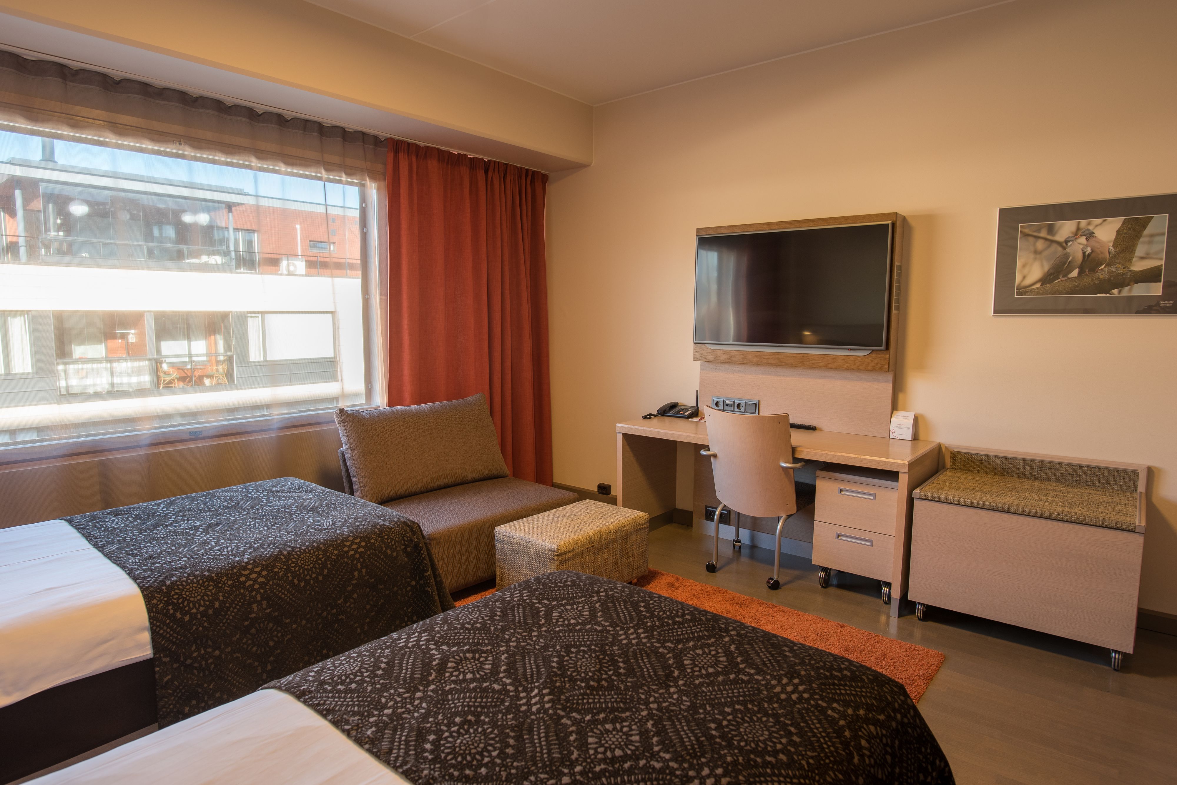 A hotel room with two beds, a desk, a chair, a TV, and a window with curtains.