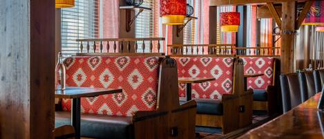 A restaurant interior with wooden booths, patterned cushions, and hanging lamps.
