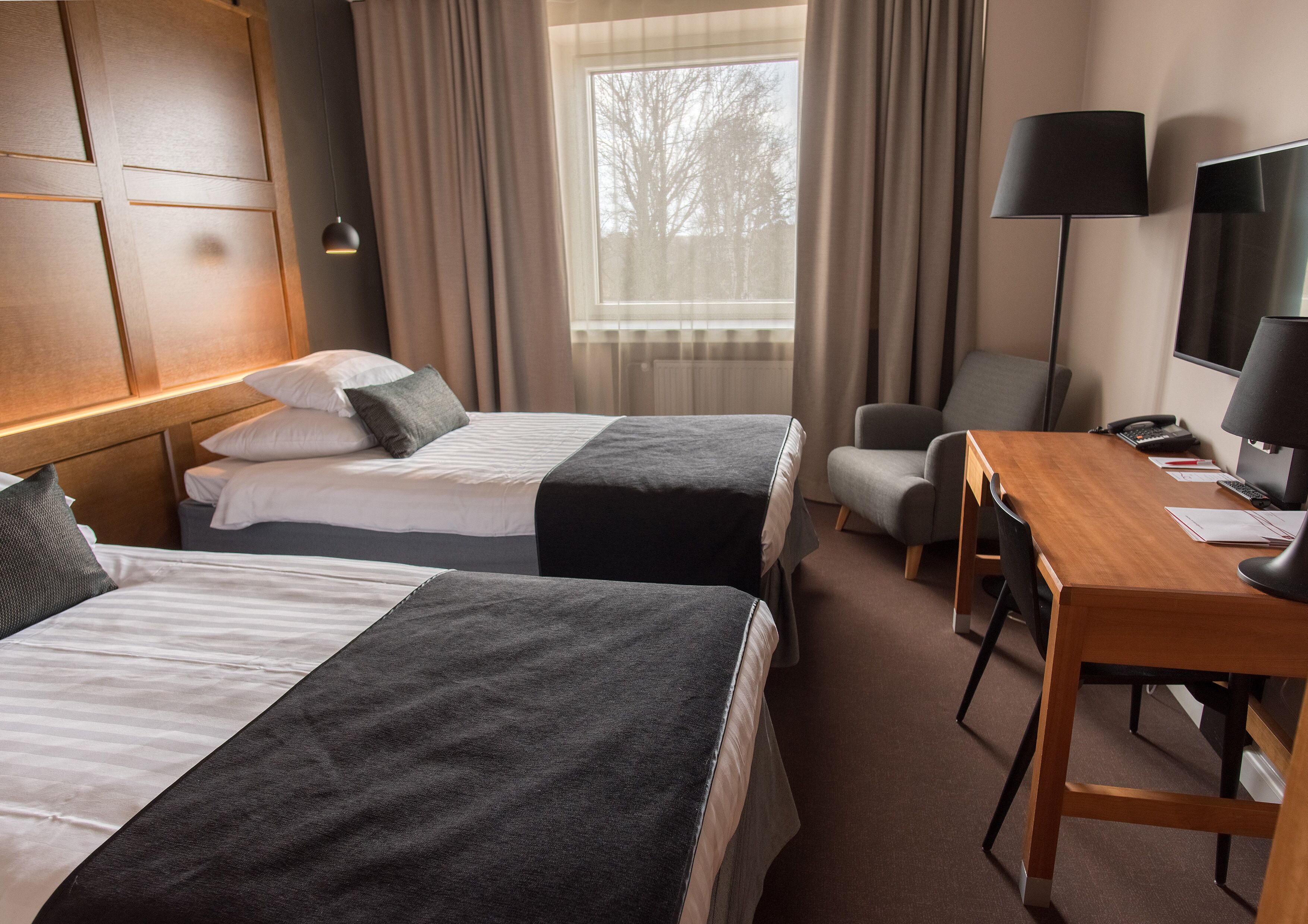A hotel room with two beds, a desk, a chair, a TV, and a window with curtains.